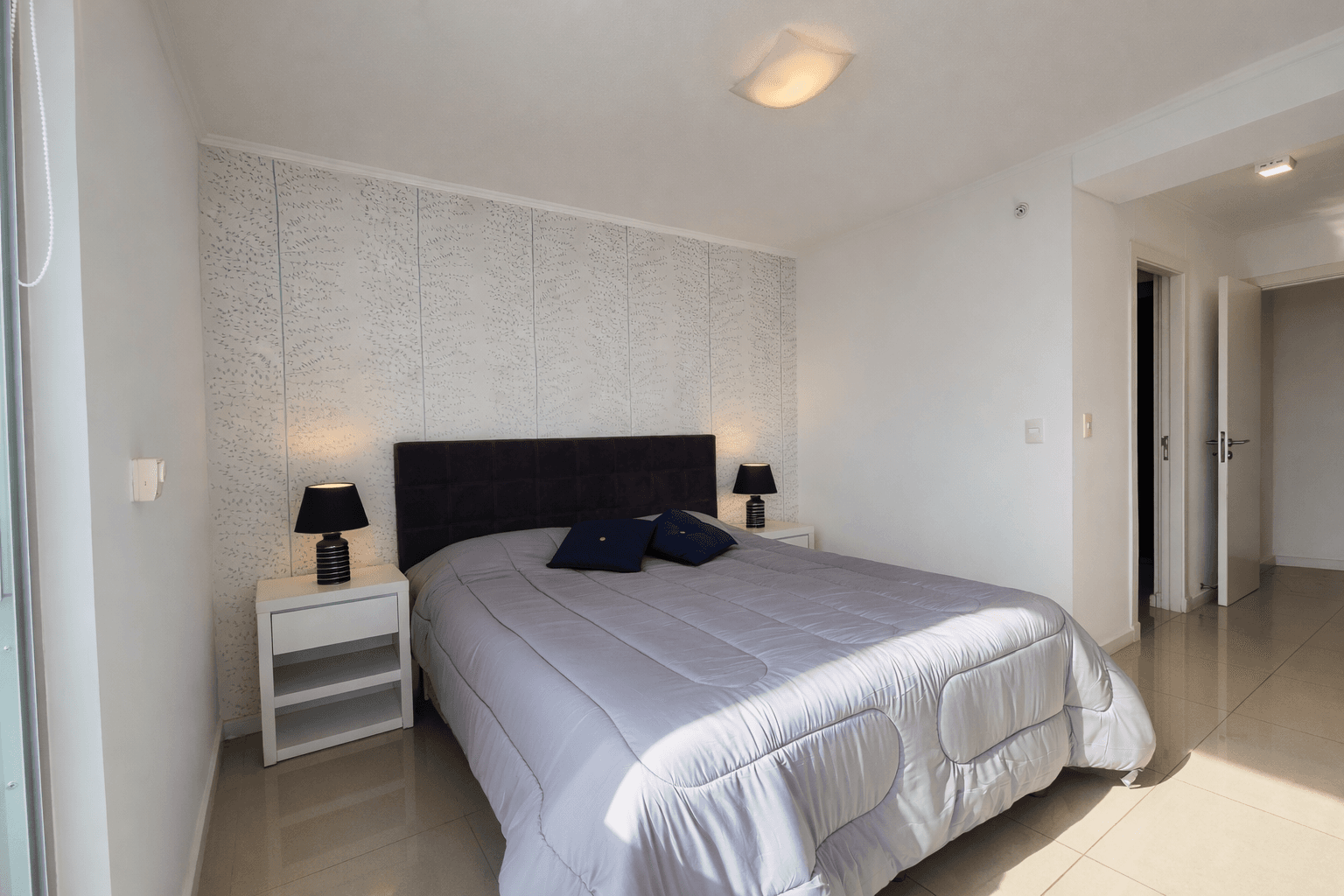 Dormitorio amplio y luminoso con cama doble, mesas de luz y grandes ventanales. Cuenta con decoración moderna en tonos neutros y buena entrada de luz natural.