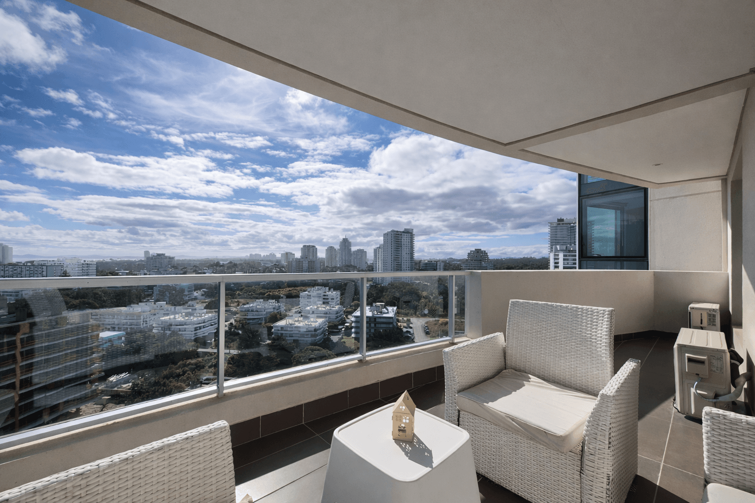 Amplio balcón con sillones de exterior, baranda de vidrio y vista panorámica a la ciudad. El espacio ofrece una vista despejada desde altura y abundante luz natural.