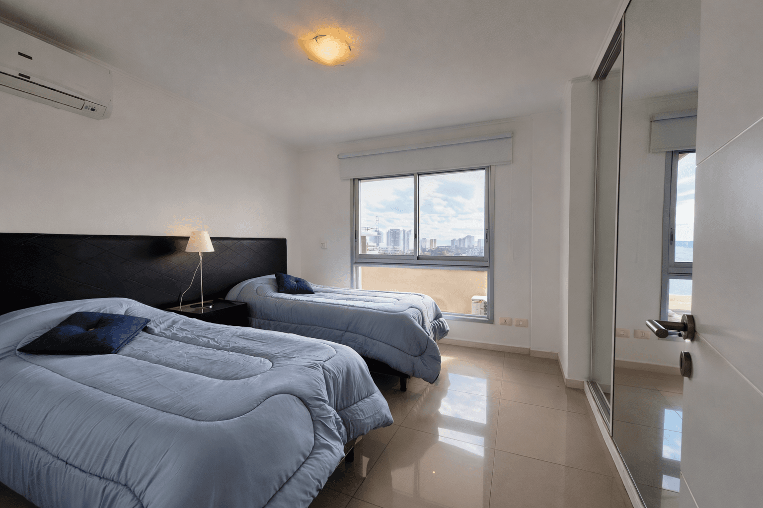 Dormitorio luminoso con dos camas individuales, aire acondicionado, amplio placard espejado y vista panorámica.