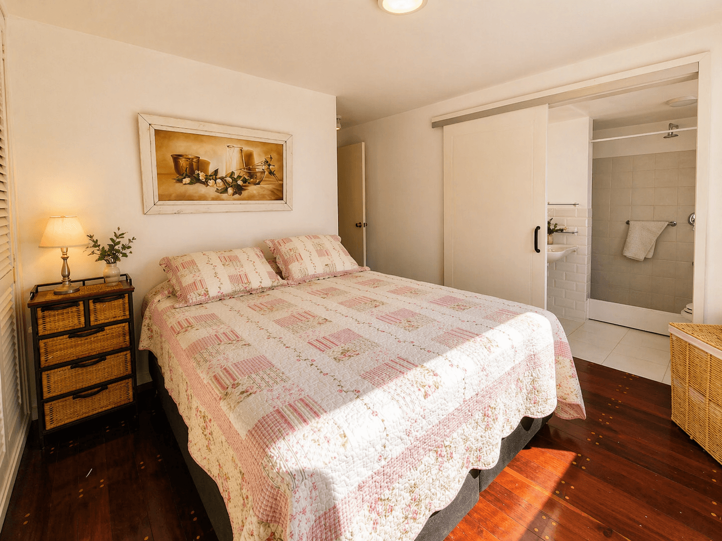 Dormitorio principal luminoso con cama doble, pisos de madera y baño en suite integrado. El baño cuenta con ducha, lavabo y espacio de guardado.