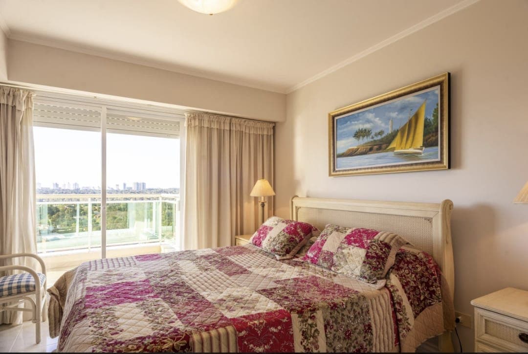 Dormitorio amplio y luminoso con cama doble, grandes ventanales y acceso directo a balcón con vista al mar. Cuenta con mesas de luz y abundante entrada de luz natural.