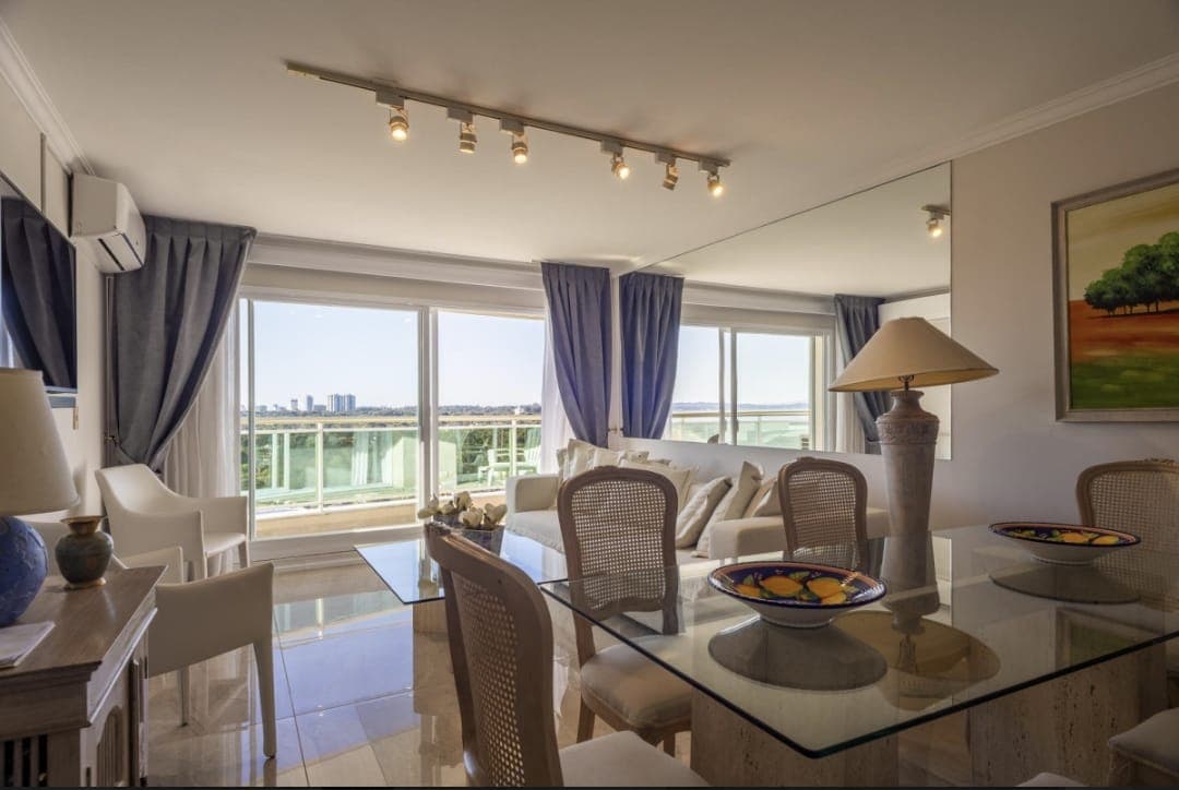 Living comedor amplio y luminoso con grandes ventanales y acceso a balcón con vista al mar. Cuenta con sofá, sillones, mesa de comedor, TV y aire acondicionado, con abundante luz natural.