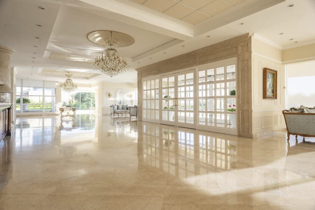 Amplio y elegante lobby de edificio residencial, con pisos de mármol, grandes ventanales, áreas de estar y lámparas de araña. El espacio cuenta con abundante luz natural y sectores de descanso.